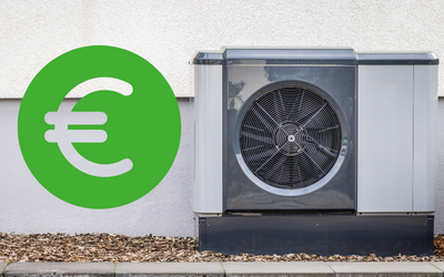Eine Wärmepumpe steht an einer Wand, daneben ist ein großes grünes Euro-Symbol. Die Pumpe hat ein graues Gehäuse und einen sichtbaren Lüfter. Der Boden ist mit kleinen Steinen bedeckt.