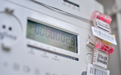 Ein digitaler Stromzähler zeigt den aktuellen Verbrauch in kWh an. Auf dem Zähler sind mehrere farbige Clips mit Barcodes angebracht. Der Bildschirm ist hell und gut lesbar, mit einer Anzeige von "000000.02 kWh".