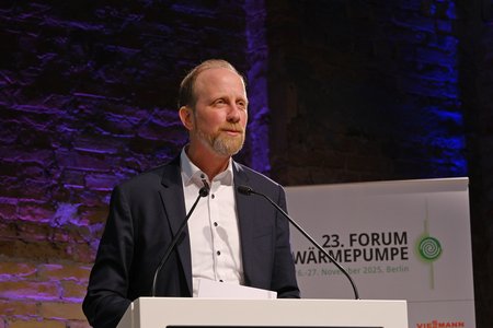 Ein Mann spricht am Podium bei einem Forum zur Wärmepumpe. Im Hintergrund ist ein Banner mit dem Titel "23. Forum Wärmepumpe" zu sehen. Die Veranstaltung findet in Berlin statt. Der Mann trägt einen Anzug und hat einen ernsthaften, konzentrierten Ausdruck.