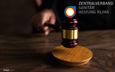 Ein Gerichtshammer wird auf einer Holzplatte geschlagen. Im Hintergrund ist das Logo des Zentralverbandes Sanitär, Heizung, Klima sichtbar. Die Hand, die den Hammer hält, ist teilweise im Bild zu sehen.